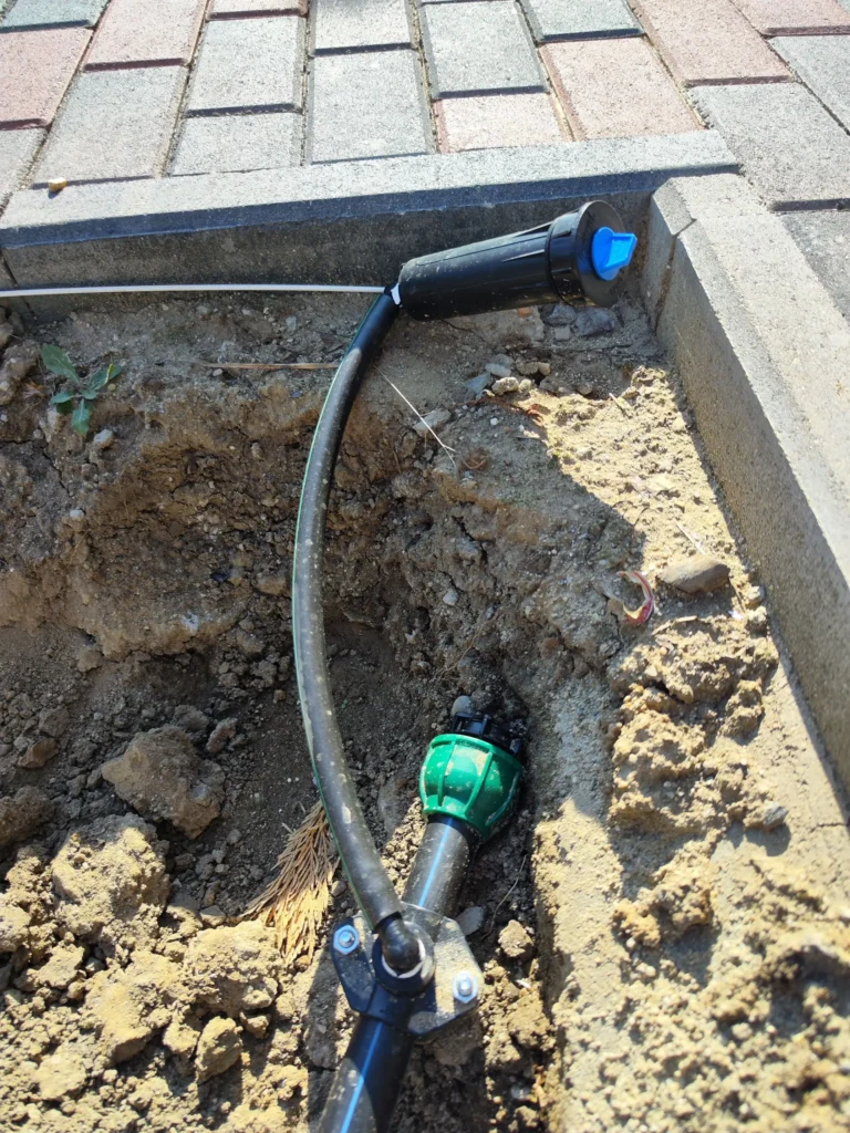 Aspersor pop-up instalat în șanț și conectat cu șa de branșament la conducta secundară a sistemului de irigații, lucrare Verdara Solutions.