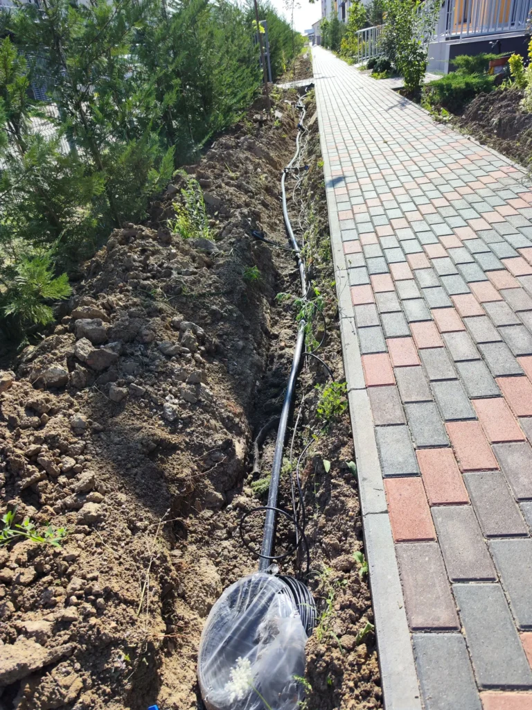 Conductă neagră PEHD pentru sistemul de irigații și cablu de comanda pentru automatizare, pozată în șanț de-a lungul spațiului verde rezidențial, lucrare Verdara.